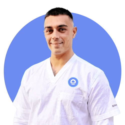 Retrato profesional de busto de un hombre joven con el cabello muy corto y oscuro, que mira a cámara con una sonrisa amable y serena. Viste un uniforme sanitario de color blanco con cuello en pico, que incluye el logotipo circular azul del centro en el lado izquierdo del pecho. El profesional aparece con los hombros relajados y ligeramente ladeado hacia la izquierda, recortado sobre un fondo circular de color azul vibrante. Debajo de la imagen, el texto identifica al profesional como Pau Bertomeu Gilabert, Terapeuta, reflejando la cercanía y profesionalidad de Bella Mar.