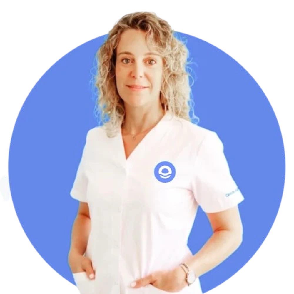 Un retrato profesional de busto de una mujer llamada Patricia, con el cabello rubio, largo y ondulado. La profesional mira fijamente a la cámara con una expresión serena y profesional. Viste un uniforme sanitario blanco de manga corta, impecablemente limpio, que incluye el logotipo circular azul de Bella Mar bordado en el lado izquierdo del pecho. Su postura es relajada, con las manos parcialmente introducidas en los bolsillos del uniforme. El retrato está enmarcado dentro de un círculo azul intenso sobre un fondo blanco, siguiendo la línea gráfica institucional del centro.