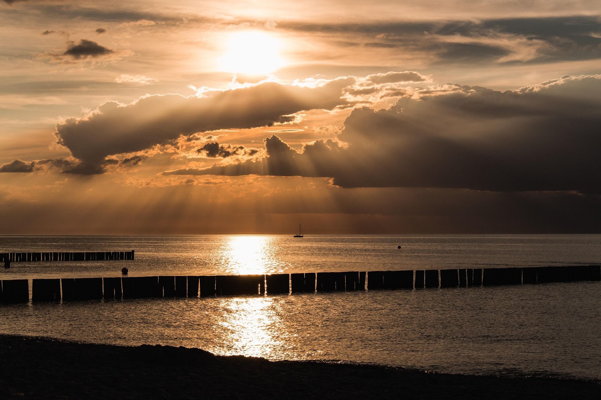 foto de un amanecer en la playa con el mar de fondo y una escala de colores beige que reina el cielo, el sol destaca y deslumbra de entre las distintas nubes que le rodea