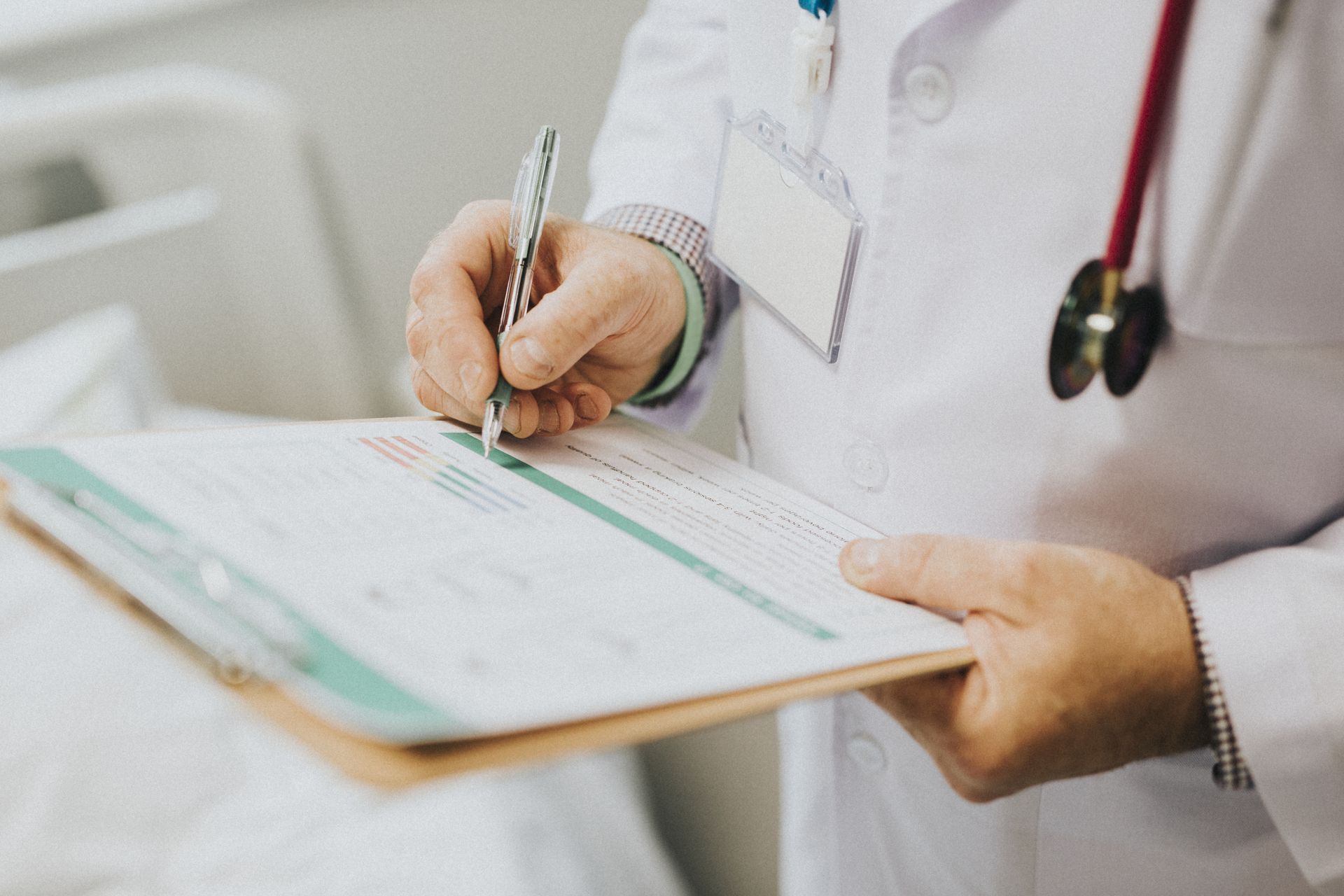 plano detalle de como un médico anota los síntomas o problemas del paciente,, se ven sus manos, unas manos ya envejecidas, una bata blanca y un carnet de identificación, imagen representativa de la importancia en el cuidado que Bella mar pone por sus pacientes