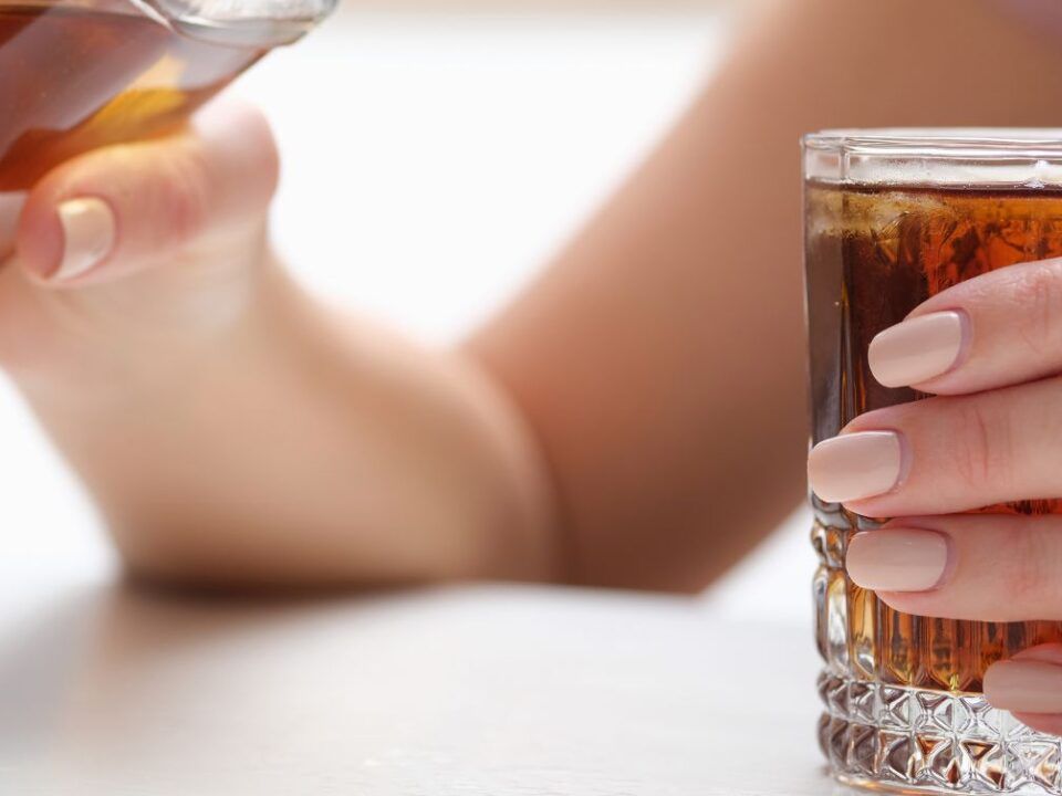 La imagen busca ilustrar los riesgos del consumo de alcohol durante la gestación y su relación con el síndrome alcohólico fetal, mostrando a la persona en un entorno cotidiano mientras consume la bebida.