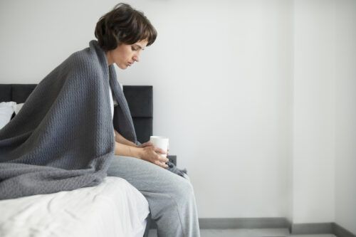 Mujer joven envuelta en una manta y sentada en la cama con mirada perdida, ilustrando las duras consecuencias de las drogas de diseño en el bienestar físico y mental.
