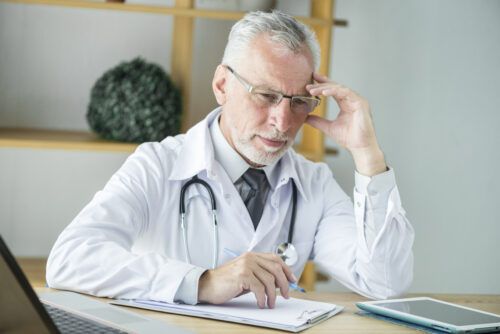 Doctor con bata blanca y estetoscopio mirando unos papeles con gesto de preocupación, representando al doctor dudando sobre la ketamina y sus riesgos en el tratamiento de adicciones.