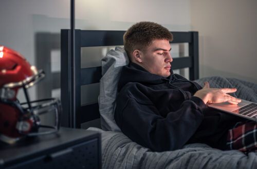 Un adolescente se sienta en su habitación sobre la cama y usa su portátil para buscar y satisfacer su deseo de pornografía