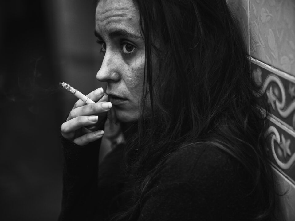 Retrato en blanco y negro de una mujer fumando con mirada perdida y expresión de angustia, representando la soledad y el impacto emocional de la drogodependencia.