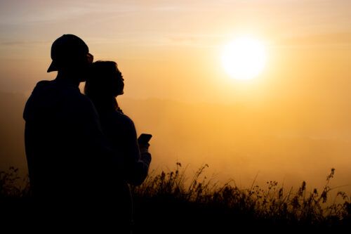 Silueta de una pareja abrazada contemplando un sol radiante desde la montaña, simbolizando el apoyo familiar en la recuperación de la adicción a la ketamina al amanecer de una nueva vida.