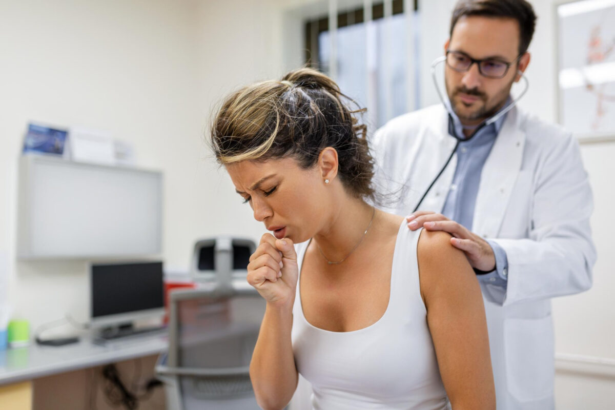 Persona tosiendo durante un examen médico mientras un profesional de la salud ausculta sus pulmones.