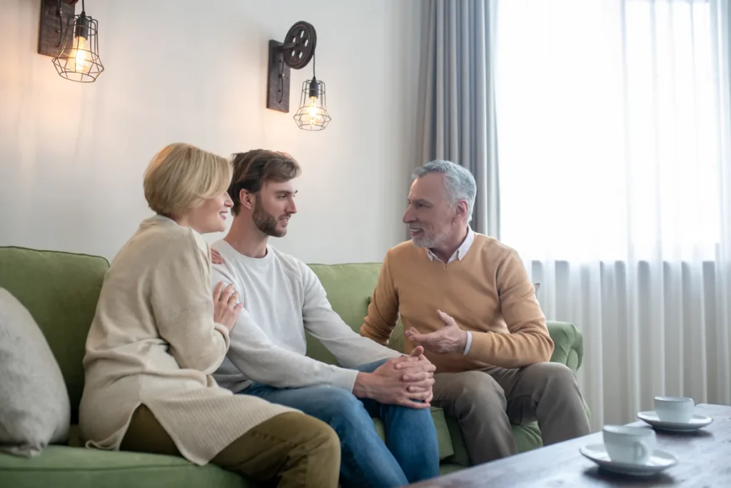 Padres conversando con su hijo adulto en el sofá de casa.