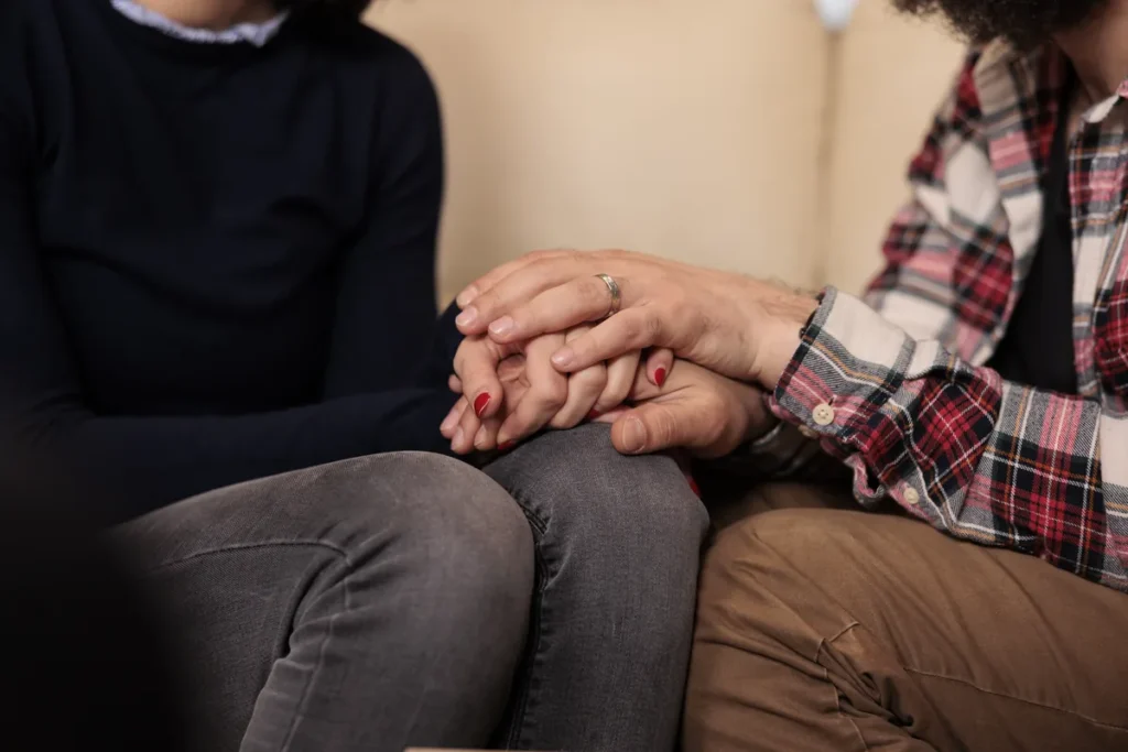 Primer plano de una pareja sosteniéndose las manos en un gesto de apoyo.